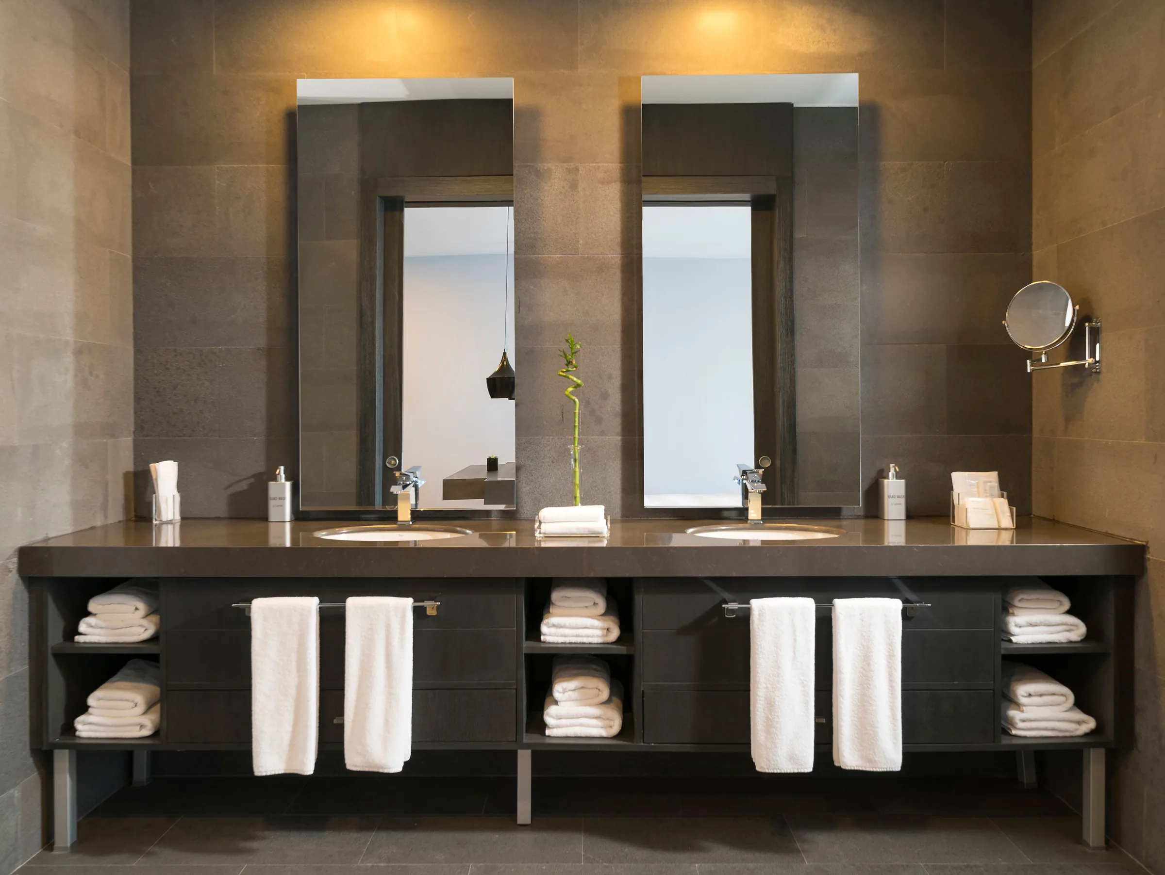 A dark stone hotel washroom with twin mirrors